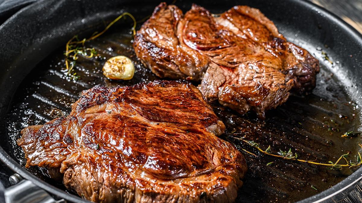 Cooked grilled marble steak Chuck roll in a pan. Dark background. Top view.