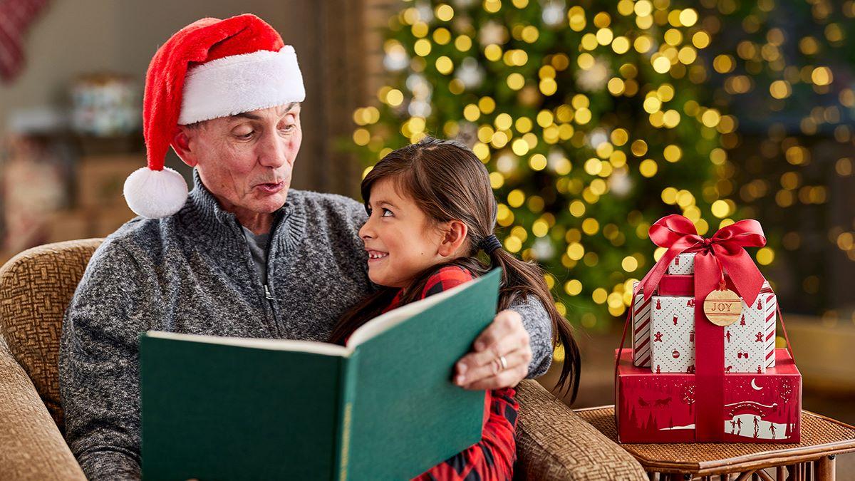 Article Cards Featured Image Grandpa wearing a santa hat reading to granddaughter    days of christmas gifts