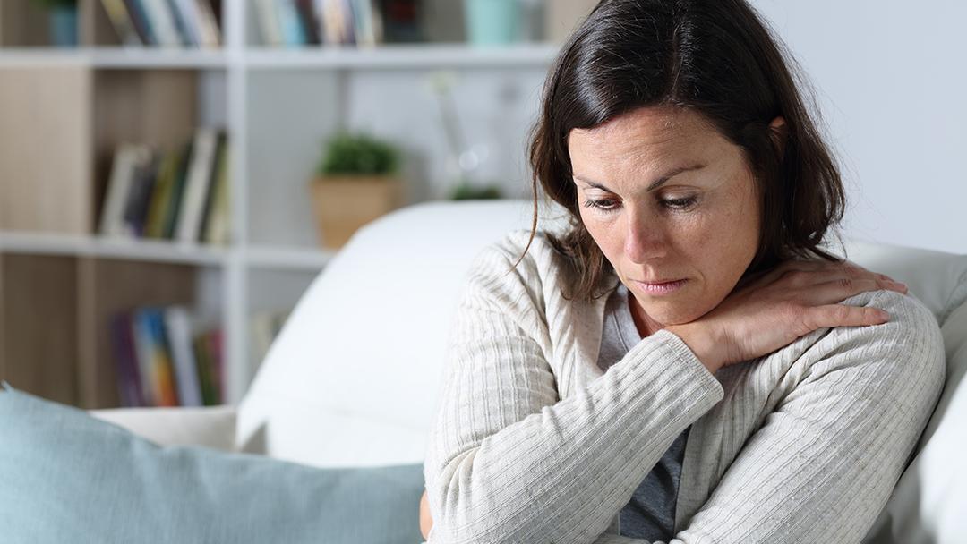 how to write an obituary with a pensive looking woman sitting at home on her couch