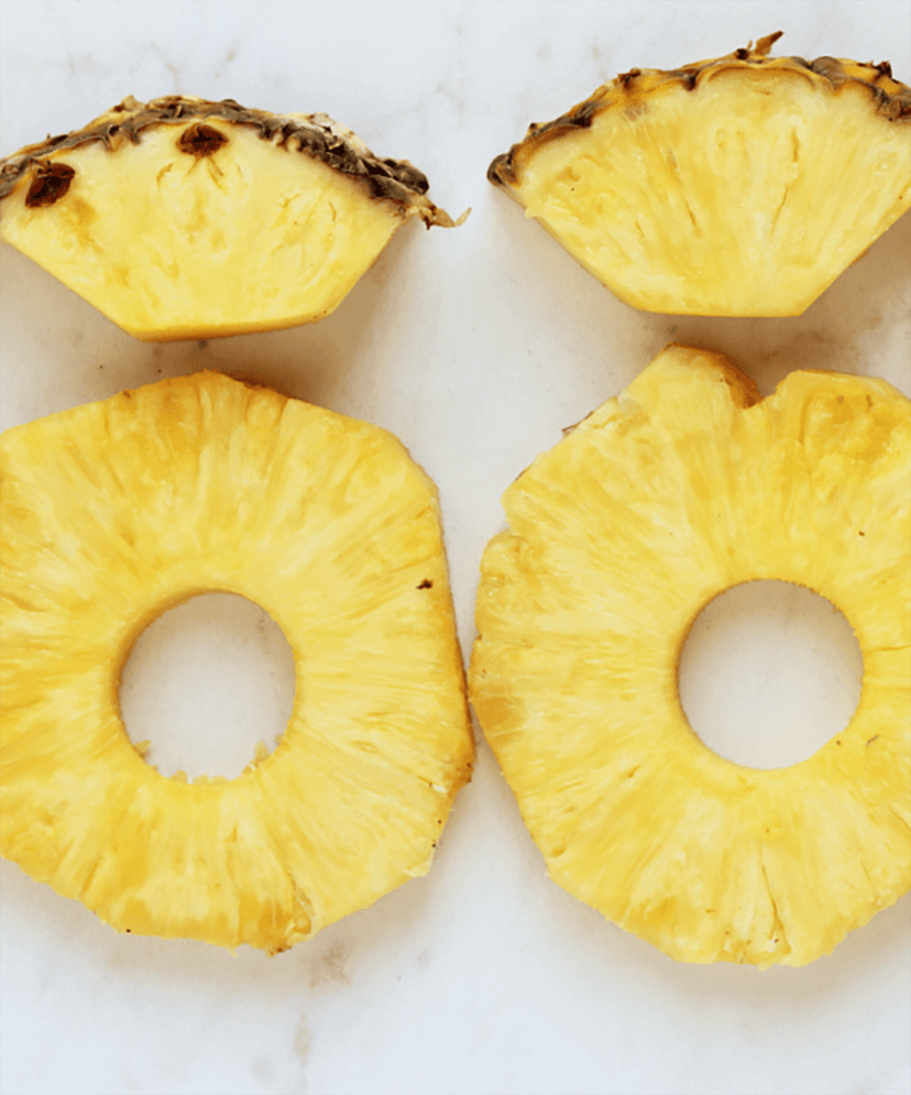 A photo of how to cut pineapple with some slices of pineapple on a counter