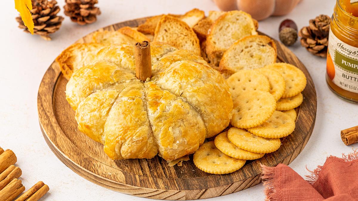 Pumpkin recipes with a baked brie en croute with pumpkin butter and candied walnuts on a platter with crackers.