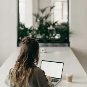 Office superstars with a woman with her back to the camera sitting at a table looking at a laptop.