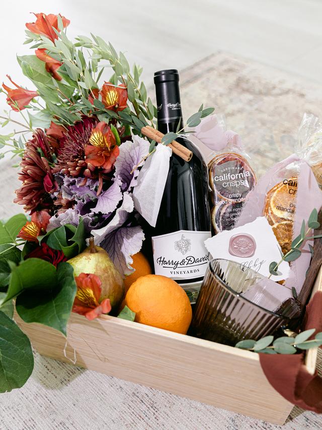 Hostess gift ideas with a basket of wine, flowers, and fruit.